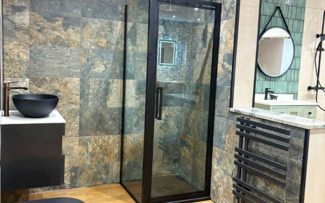 A clean bathroom showroom layout showcasing a modern shower, basin, and toilet against a stylish stone-like wall.