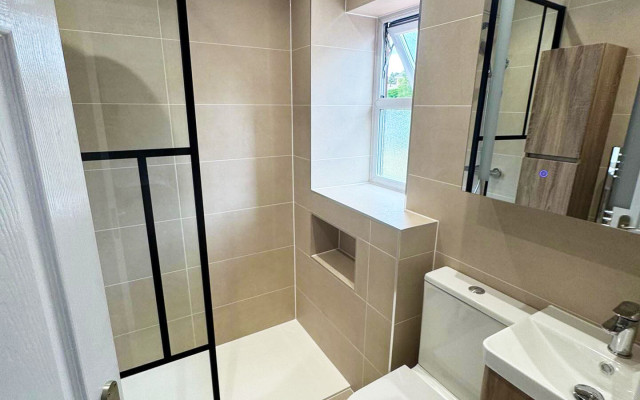 A clean bathroom featuring a shower, toilet, and basin, with neutral-coloured tiles and bright lighting.