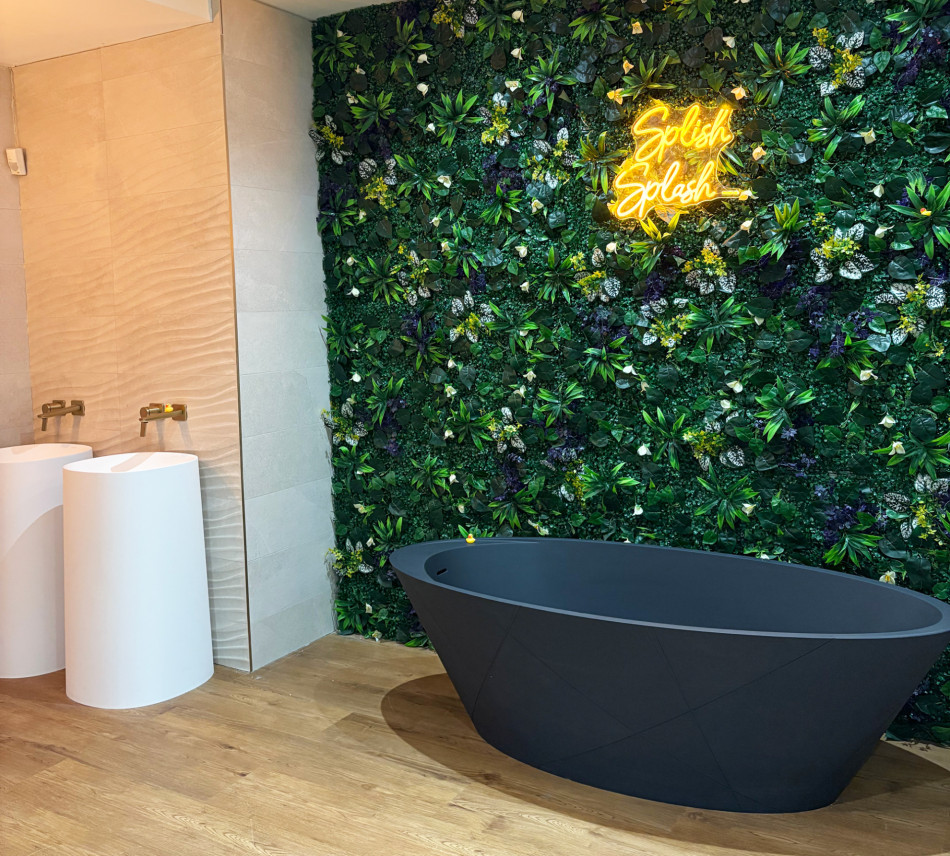 A modern bathroom featuring a vibrant green wall and a sleek black bathtub, enhanced by glowing neon signage that reads 'Splash Splash'.