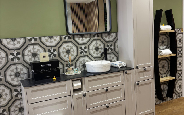 A clean bathroom featuring a white toilet, stylish basin, and elegant wooden cabinet, complemented by distinctive geometric tiles and a modern colour palette.